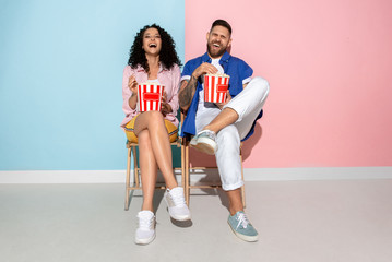 Fototapeta na wymiar Young emotional caucasian couple in bright casual clothes posing on pink and blue background. Concept of human emotions, facial expession, relations, ad. Man and woman watch cinema with popcorn.