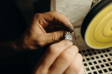 Crafting. Hands of the jeweler polishes silver jewelry brooch on the polishing wheel. Little gain...