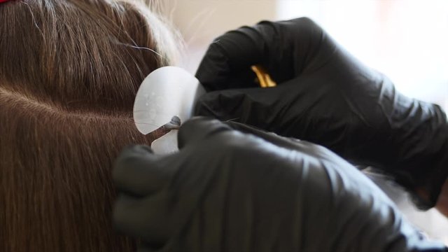 A hairdresser with two hands in black gloves is slowly preparing for hair extension for the woman client at the hair studio. Action of extension is close up.