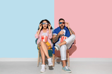 Young emotional caucasian couple in casual clothes posing on pink and blue background. Concept of human emotions, facial expession, relations, ad. Man and woman watch cinema with popcorn, look shocked