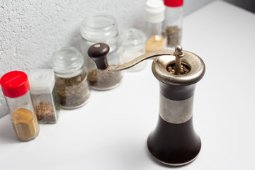 Ancient pepper mill near another seasonings on white background.