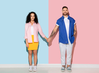 Young emotional caucasian couple in bright casual clothes posing on pink and blue background. Concept of human emotions, facial expession, relations, ad. Man and woman holding hands, smiling.