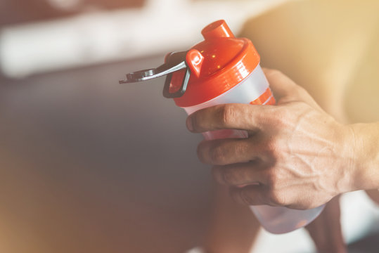Close up of man's hand holding a classic fitness shaker with pre-workout drink in it. Sports nutrition concept. Horizontal shot
