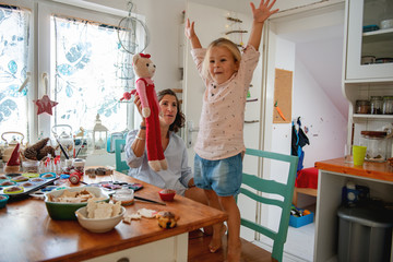 Mother and daughter playing with teddy bear in the kitchen