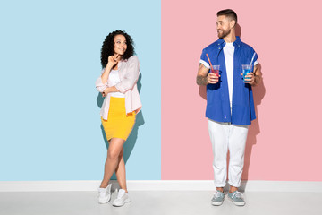 Obraz premium Young emotional caucasian couple in bright casual clothes posing on pink and blue background. Concept of human emotions, facial expession, relations, ad. Man and woman going to drink cocktails.