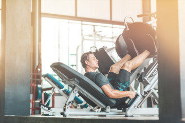 Portrait of young male athlete looking aside while using a training machine. He is doing leg...