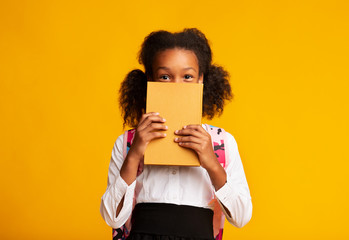 Black Schoolgirl Hiding Behind Book Over Yellow Background