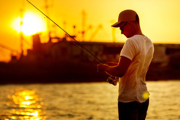 Young man fishing at sea from the shore at sunset. soft light. fisherman uses spinning