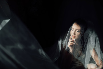 Portrait of charming bride enveloped in a veil. Beuatiful bride hidden under the veil. Beautiful bride in veil. Close up. Beauty woman. Wedding morning closeup on black background.