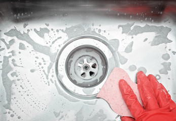 Top view of sink drain and hand wearing orange rubber glove