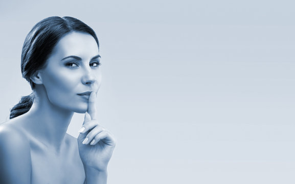 Blue tone vintage beauty portrait of young woman keeping finger on her lips and asking to keep quiet