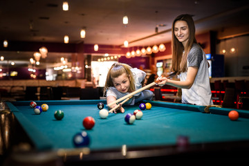 Beautiful woman with her friend playing billiard in pub
