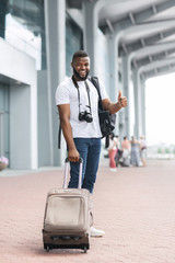 Fototapeta na wymiar Happy african american guy with suitcase showing thumb up at airport