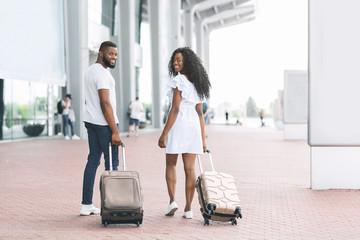 Happy couple arriving at airport, pulling suitcases