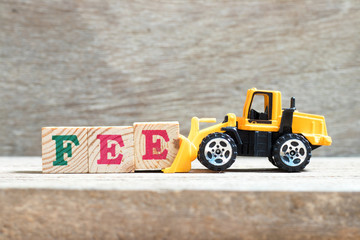 Toy bulldozer hold letter block e to complete word fee on wood background