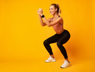 Millennial Girl Doing Deep Squat Exercise On Yellow Background