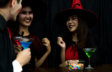 Group of young Asian people in Halloween costume sitting on table with candy and nectar at Halloween party in dark background