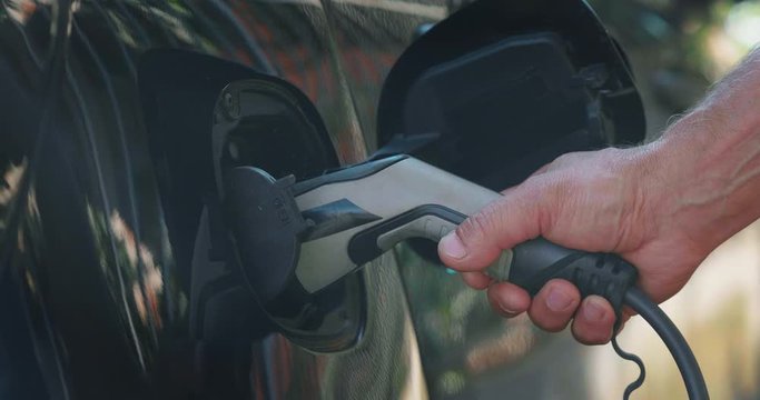Slow motion close up of power supply plugged into an electric car for charging a modern battery which is the future of the automobile and new era of vehicle fuel on the street.