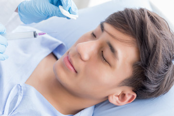 Cosmetology. Portrait Of Asian Handsome Man With Perfect Skin Getting Beauty Treatment in clinic. Closeup Of doctor Hands Injecting Filler Injection On Male Face.