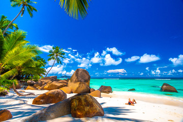 Woman sunbathing in a typical beach in Seychelles with granite rocks - obrazy, fototapety, plakaty