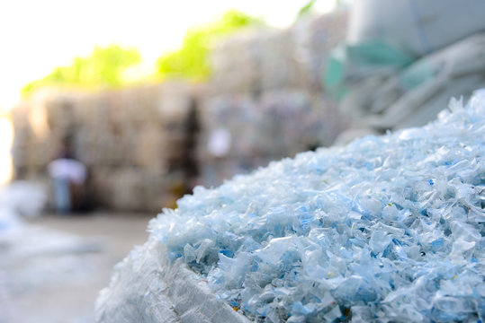 Close Up PET Plastic Bottle Flakes In White Big Bag With Blur Plastic Bottle Bales Background 