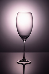 Transparent  glass goblet without wine on a thin leg stands on a mirror surface.