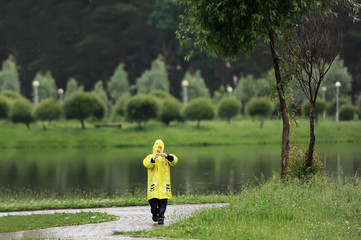 Child in a yellow raincoat alone is in city park.