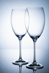 Two glass goblet without wine on a thin leg stands on a mirror surface.