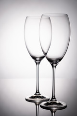 Two glass goblet without wine on a thin leg stands on a mirror surface.
