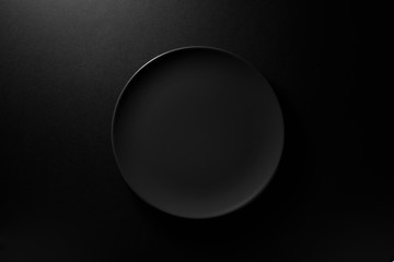 Empty round black plate on dark moody black background with copy space. Overhead view