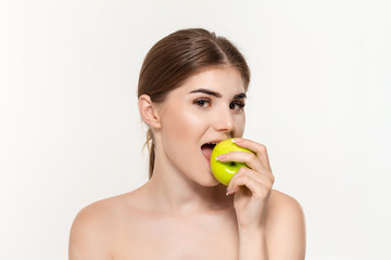 Obraz na płótnie Canvas Close-up portrait of a happy beautiful young girl biting green apple isolated over white background. Concept of beauty and health care.