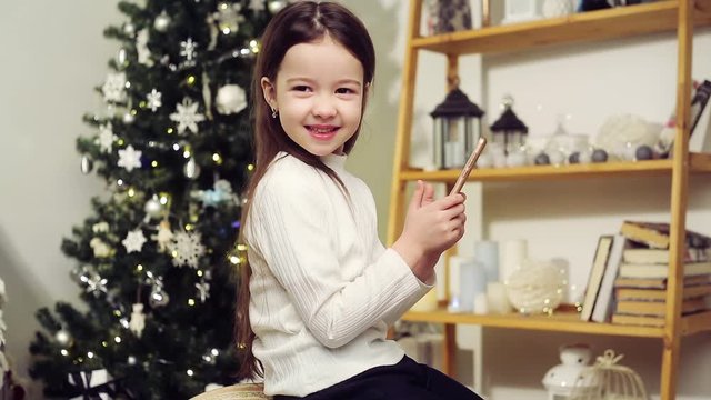 Cute girl with a phone on the background of the Christmas tree