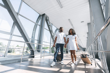 African newlyweds walking with suitcases at airport terminal