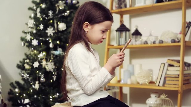 Cute girl with a phone on the background of the Christmas tree