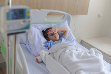 Patient child laying on hospital bed with blurred saline solution drip and infusion pump equipment