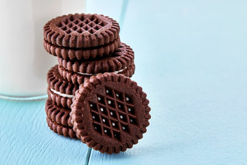 Round chocolate biscuits filled with cream and a bottle of milk on blue wooden table. Macro view.
