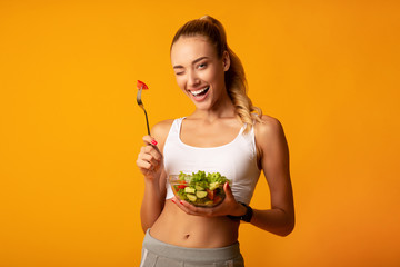 Girl Eating Salad Winking At Camera Over Yellow Background