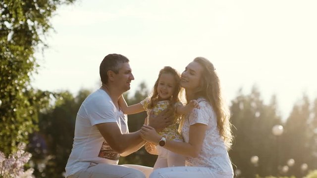 Happy young family with a daughter at sunset. Portrait with a warm atmosphere. The soft rays of the sun glare. Slow motion.