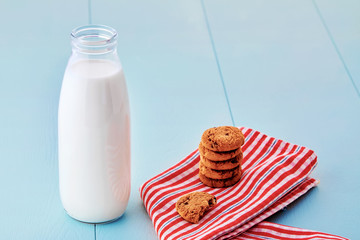 Bottle of milk and pile of chocolate chip cookies on napkin on blue wooden table. Close up view from above.