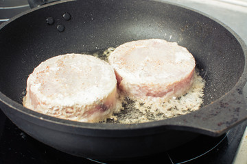 Raw pieces of fish fillet hake fried in skillet on stove.