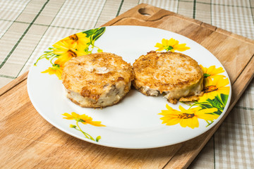 Fried round hake fish fillets in plate on kitchen table.