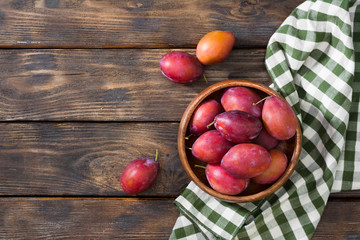 Red plums in a wooden bowl on a wooden table. Rustic style