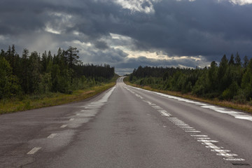 Road across Swedish Lapland is lit with ray of sunlight from under a thundercloud