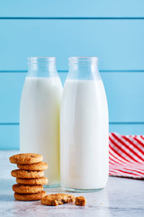 Two bottles of milk and chocolate chip cookies on wooden table with blue wooden background.