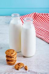 Two bottles of milk and chocolate chip cookies on wooden table with blue wooden background.