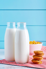Milk bottles, chocolate chip cookies and a bowl of cereal on wooden table with turquoise wooden background