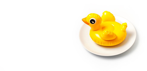 Inflatable mini yellow chicken or duckling on white plate on white background. Creative food concept, tobacco chicken. Flat lay copy space. Trend Inflatable Children toy for swimming Layout for design