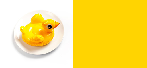 Inflatable mini yellow chicken or duckling on white plate on white background. Creative food concept, tobacco chicken. Flat lay copy space. Trend Inflatable Children toy for swimming Layout for design