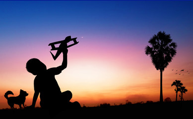 Silhouette of kid dreams as pilot sitting and holding airplane paper with friend running with wind turbine in sunset, imagination and freedom  idea concept