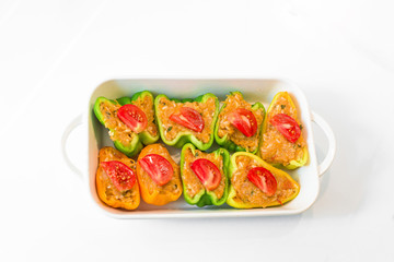 stuffed pepper halves in a white baking bowl . yellow and green pepper with tomatoes